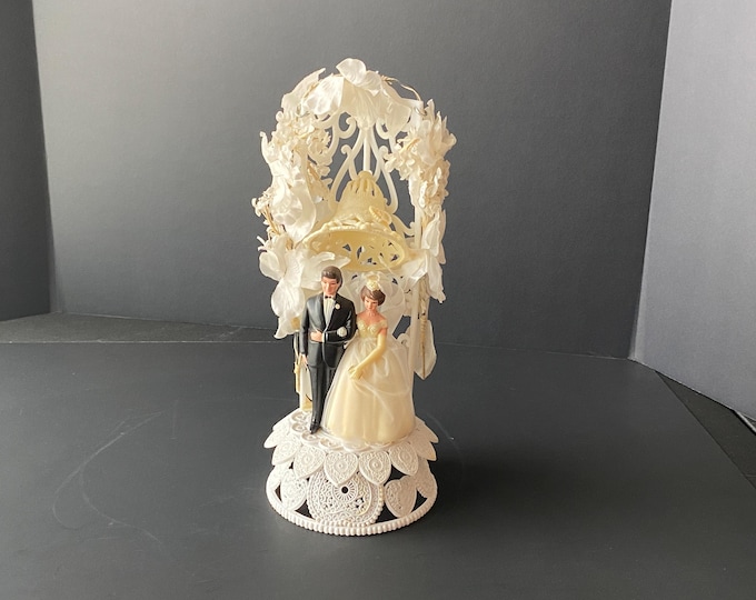 Vintage Plastic Bride and Groom Cake Topper with Plastic Trellis surrounded by White Flowers and Sugared Wedding Bell From Wilton