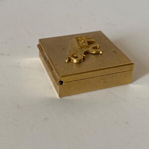 Puede incluir: Peque&ntilde;a caja rectangular dorada con una figura de caballo en relieve en la tapa. La caja tiene un dise&ntilde;o con bisagras y parece estar hecha de metal. La figura del caballo tambi&eacute;n es dorada y a&ntilde;ade un elemento decorativo.