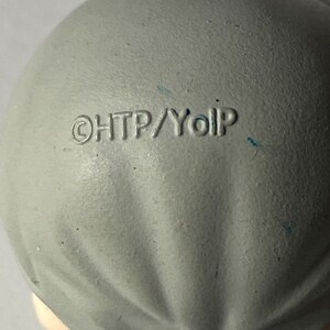 May include: Close-up of a gray, rounded object with the text "&copy;HTP/YoIp" imprinted on its surface. The object has a textured appearance and appears to be made of a matte material. The overall shape is smooth and slightly irregular.