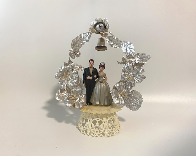Vintage  25th Silver Anniversary Bride and Groom Cake topper beneath an arch of Silver Foils flowers and Bell on Plastic Filigree Pedestal