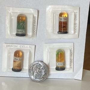 May include: Four miniature glass vials with black bases, each containing a different substance and labeled. The labels read "SNAKEROOT", "TOAD STOOL", "BRAIN CELLS", and "MOON JELLY". A U.S. dime is included for size reference.
