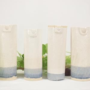 May include: Four white ceramic vases with a blue glaze at the bottom. The vases have a unique, textured surface and a small, rounded opening at the top.