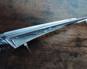May include: A chrome car hood ornament in the shape of a bird with a long, pointed beak. The ornament is mounted on a wooden surface.