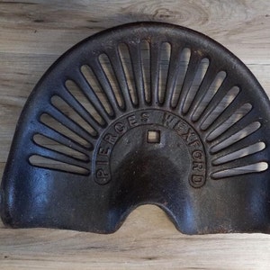 Könnte beinhalten: Ein schwarzer Traktorsitz aus Gusseisen mit einem dekorativen Design und den eingeprägten Worten "PIERCE'S WEXFORD" auf der Vorderseite.