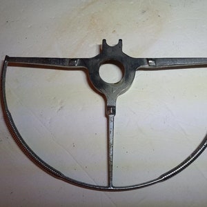 May include: A silver metal steering wheel frame with a spring-loaded design. The frame is designed to fit over a steering wheel and is used to hold a steering wheel cover in place.