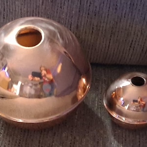 Puede incluir: Dos objetos esféricos de color cobre con una superficie reflectante. La esfera más grande tiene un diámetro de aproximadamente 13 cm, mientras que la más pequeña mide unos 8 cm de diámetro. Ambos tienen un agujero en la parte superior.