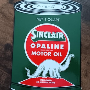 Puede incluir: Un letrero metálico vintage que anuncia el aceite de motor Sinclair Opaline. El letrero tiene forma de lata y presenta una ilustración de dinosaurio roja y blanca. El texto en el letrero dice "NET 1 QUART", "SINCLAIR", "OPALINE", "REG U.S. PAT. OFF", "MOTOR OIL", "MELLOWED" y "80 MILLION YEARS".