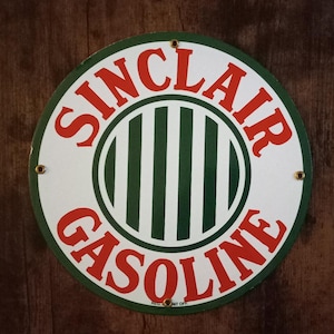 Puede incluir: Un letrero vintage redondo de metal blanco con un círculo de rayas verdes y blancas en el centro. El letrero dice "Sinclair Gasoline" en letras rojas alrededor del círculo.