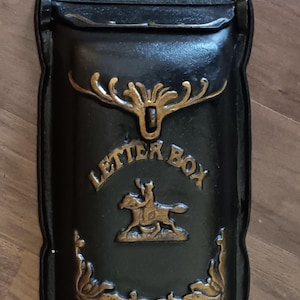 May include: Black metal letterbox with gold detailing. The letterbox features the words "LETTER BOX" and a depiction of a rider on horseback. The design is rectangular with a curved top and decorative flourishes.