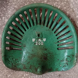 Könnte beinhalten: Ein antiker grüner Traktorsitz mit geschlitztem Design. Der Sitz hat den weißen Text "W.A.W 208". Der Sitz ist aus Metall und weist Gebrauchsspuren und Alter auf.
