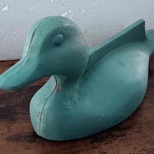 May include: A teal blue ceramic duck figurine. The duck has a long, slender beak and a rounded body.