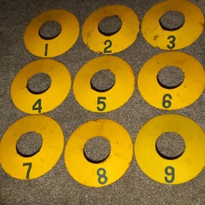 May include: Nine yellow circular targets with numbers 1 through 9 printed in green on them. The targets are arranged in a 3x3 grid.