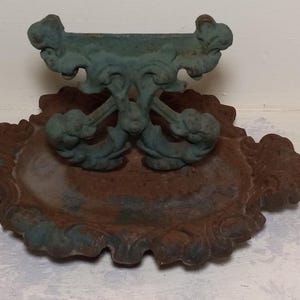 May include: A vintage cast iron boot scraper with a decorative design. The scraper has a green patina and is in good condition.