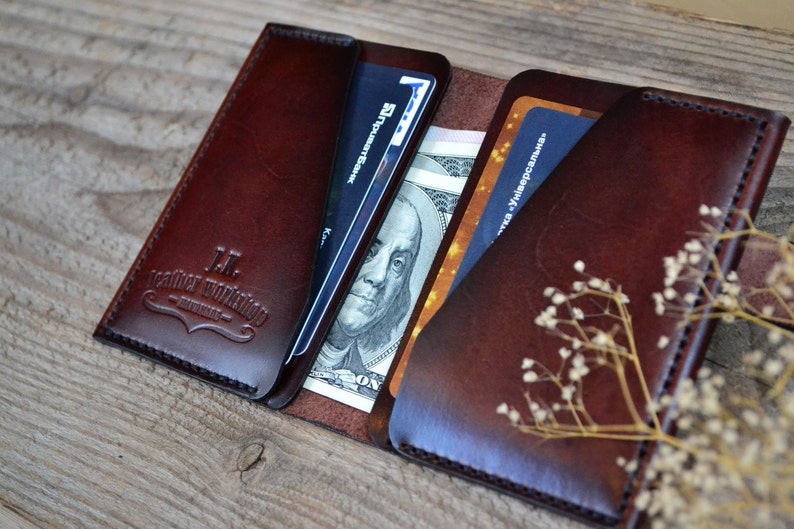 May include: A brown leather wallet with a stitched edge and the text "H.L. Leather Workshop" embossed on the front. The wallet is open, revealing a credit card, cash, and another card.