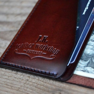 May include: A brown leather wallet with the text "J.K. Leather Workshop - Handmade" embossed on the front. The wallet is open and shows a credit card and a dollar bill.