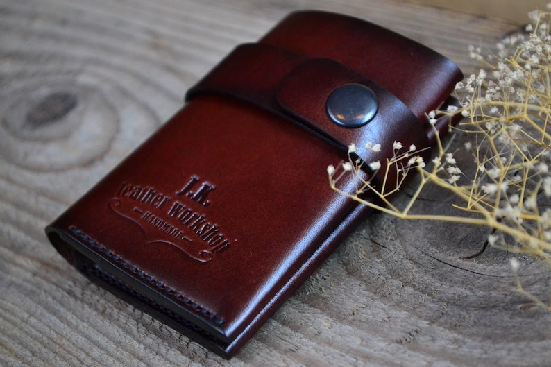 May include: A brown leather wallet with a snap closure and the text "J.K. Leather Workshop - Handmade" embossed on the front.