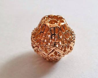May include: A gold-colored metal bead with a delicate, intricate design. The bead is round and has a hollow center.