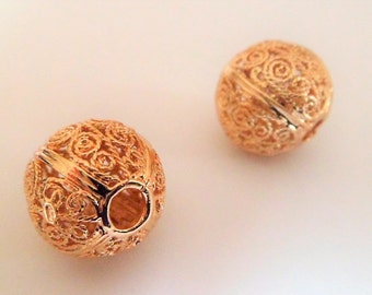 May include: Two gold-colored metal beads with intricate filigree designs. The beads have a round shape and a hole in the center.