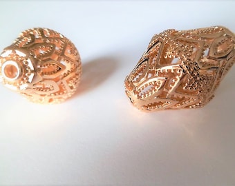 May include: Two gold-colored, openwork beads. One is spherical, the other is an elongated, irregular shape. Both have intricate geometric patterns and a metallic sheen, suggesting they are made of metal.