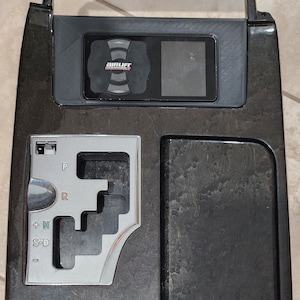 May include: A dark wood-grain car console with a silver gear shift and an Air Lift Performance display. The console has a rectangular shape with a curved bottom edge and a rectangular storage area.