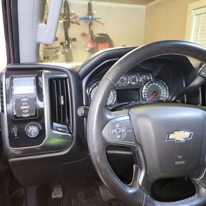 May include: The interior of a black pickup truck with a black leather steering wheel, a black dashboard, and a black and silver center console. The steering wheel has a silver Chevrolet logo in the center.