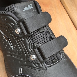 May include: Black athletic shoe with velcro straps and a mesh panel. The shoe has a silver logo that says "AVA" on the side.
