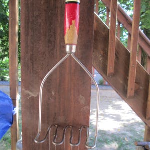 May include: A handmade wind chime with a red and black painted wooden handle, silver metal frame, and dangling beads. The beads are a mix of black and red, adding a decorative touch to the outdoor decor.