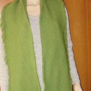 May include: A green knitted hooded scarf with a long, pointed design. The scarf is made of a soft, textured yarn and has a loose, flowing fit.