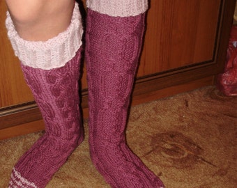 May include: A pair of long, knitted socks with a pink and burgundy color scheme. The socks have a cable knit pattern and a pink cuff.
