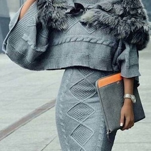 Peut inclure: Un ensemble de pull et jupe en tricot gris à motif torsadé. Le pull est orné d'une bordure en fourrure autour du col et des épaules. La femme porte des lunettes de soleil.