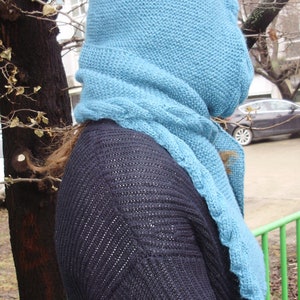 May include: A blue knitted scarf and hood with a black knitted sweater underneath.