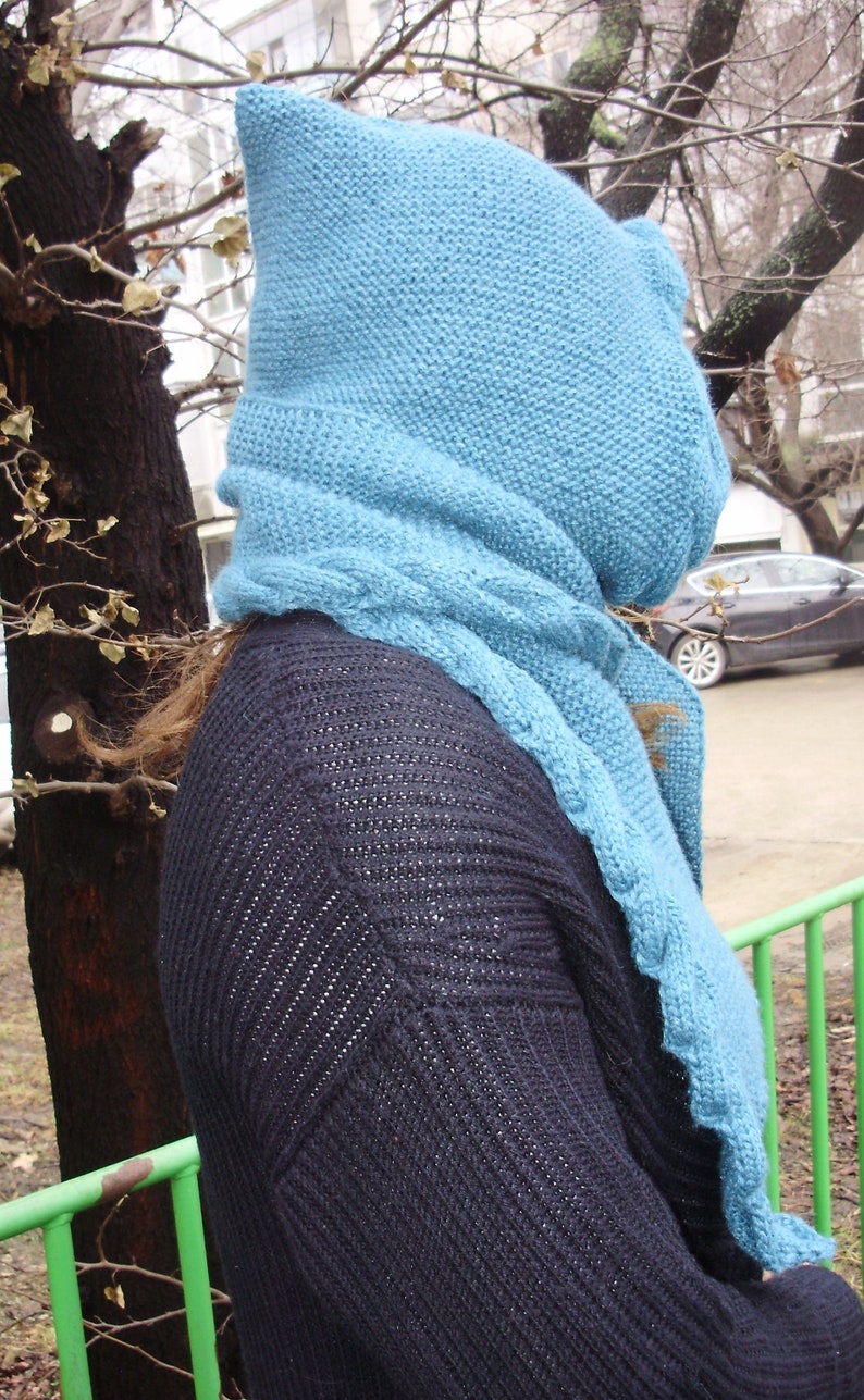 May include: A blue knitted scarf and hood with a black knitted sweater underneath.