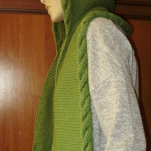 May include: A green knitted hooded scarf with a cable knit pattern. The scarf is worn by a person with dark hair.