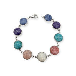 Könnte beinhalten: Ein silbernes Armband mit einer Reihe farbiger, kreisförmiger Steine in den Farbtönen Blau, Lila, Türkis, Rosa und Weiß. Die Steine sind in einzelnen Silberfassungen gefasst und durch kleine Silberglieder verbunden. Das Armband hat einen Karabinerverschluss.