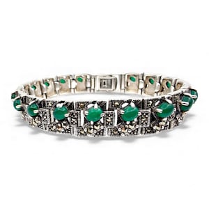 Könnte beinhalten: Silberfarbenes Armband mit quadratischen Gliedern, die mit kleinen, runden, grünen Edelsteinen und winzigen, funkelnden Akzenten besetzt sind. Das Armband liegt vor weißem Hintergrund.