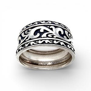 Könnte beinhalten: Ein silberner Ring mit einem breiten Band, das ein detailliertes, wirbelndes, schwarz-silbernes Muster aufweist. Der Ring hat eine polierte Oberfläche und ein klassisches Design, das für den Alltag oder besondere Anlässe geeignet ist.