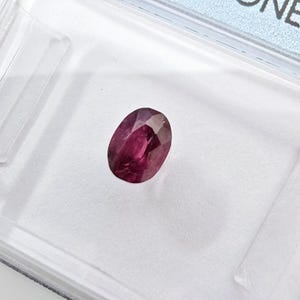 Könnte beinhalten: Ein ovaler Edelstein in tiefroter Farbe mit einem leichten violetten Schimmer.