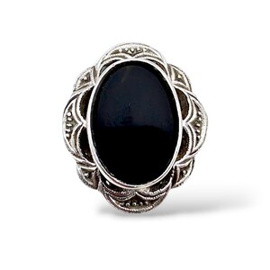Könnte beinhalten: Ein silberner Ring mit einem ovalen, schwarzen Stein in der Mitte. Der Ring hat ein verziertes, blumeninspiriertes Design um den Stein herum. Der Schmuck ist vor einem weißen Hintergrund platziert, der die Details hervorhebt.