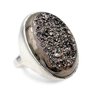 Könnte beinhalten: Ein Silberring mit einem großen, oval geformten, dunkelgrauen Stein. Der Stein hat ein strukturiertes, kristallines Aussehen. Der Ring hat ein glattes, breites Band mit gehammerter Textur an den Seiten.