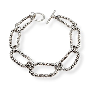 Könnte beinhalten: Ein silbernes Armband mit einem strukturierten Kettendesign. Das Armband hat einen Knebelverschluss und eine Reihe von miteinander verbundenen ovalen Gliedern. Die Glieder bestehen aus kleinen, eng beieinander liegenden Perlen.