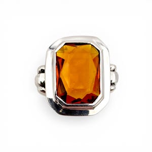 Könnte beinhalten: Ein silberner Ring mit einem großen, rechteckigen, bernsteinfarbenen Edelstein. Der Edelstein ist in einer silbernen Lünette mit rechteckiger Form gefasst. Der Ring hat ein schlichtes, aber elegantes Design, das für jeden Anlass geeignet ist.