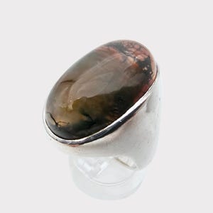 Puede incluir: Un anillo de plata con una gran piedra preciosa de forma ovalada. La piedra preciosa es una mezcla de colores marr&oacute;n, verde y rosa con un patr&oacute;n de remolino.