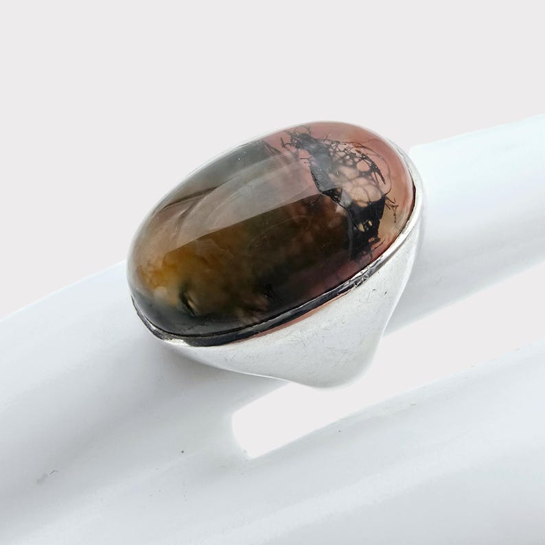 Puede incluir: Un anillo de plata con una gran piedra preciosa de forma ovalada. La piedra preciosa es una mezcla de marr&oacute;n, verde y rosa con patrones dendr&iacute;ticos negros.