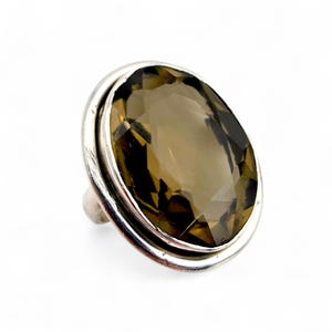 Könnte beinhalten: Ein Silberring mit einem großen, oval geschliffenen Rauchquarz-Edelstein. Der Edelstein hat eine facettierte Oberfläche und einen warmen, braunen Farbton. Der Ring hat ein schlichtes, poliertes Silberband.
