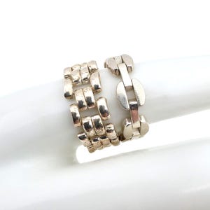 Könnte beinhalten: Ein silberfarbener Ring mit geometrischem Design. Der Ring hat eine Reihe rechteckiger und ovaler Glieder, die einen kühnen, modernen Look erzeugen. Der Ring wird vor weißem Hintergrund gezeigt.