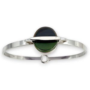 Può includere: Un braccialetto argentato con una pietra ovale al centro, che mostra tonalità verde scuro e nero. Il braccialetto ha un design semplice ed elegante con una chiusura a fermaglio.