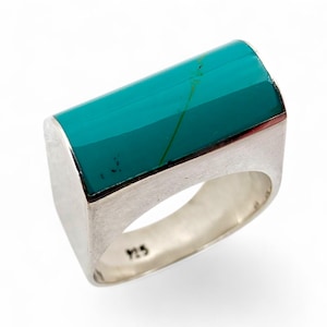 Könnte beinhalten: Rechteckiger Ring mit einem leuchtend türkisfarbenen Stein in einem silbernen Band. Der Stein hat eine grüne Ader. Der Ring ist Größe 9.5. Das Design ist modern und auffällig.