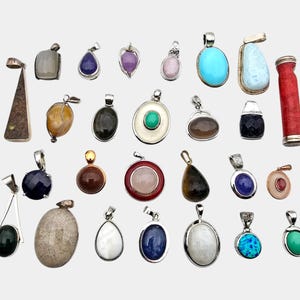 May include: A selection of gemstone pendants in diverse shapes and colours, such as turquoise, amethyst, and onyx. Each pendant is unique, with silver-toned metal settings. The assortment includes oval, teardrop, and rectangular designs.
