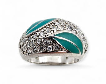 Puede incluir: Un anillo plateado con un diseño abovedado. El anillo presenta dos acentos de esmalte en forma de hoja de color turquesa y está incrustado con numerosas piedras preciosas pequeñas y claras. Las piedras preciosas cubren la parte superior del anillo.