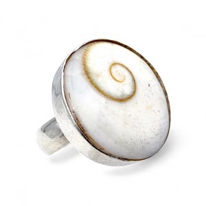 Könnte beinhalten: Silberring mit einer großen, ovalen, weißen Muschel, die ein auffälliges Spiralmuster in Braun- und Beigetönen aufweist. Der Ring hat ein breites, poliertes Silberband und ein schlichtes, elegantes Design für den täglichen Gebrauch.